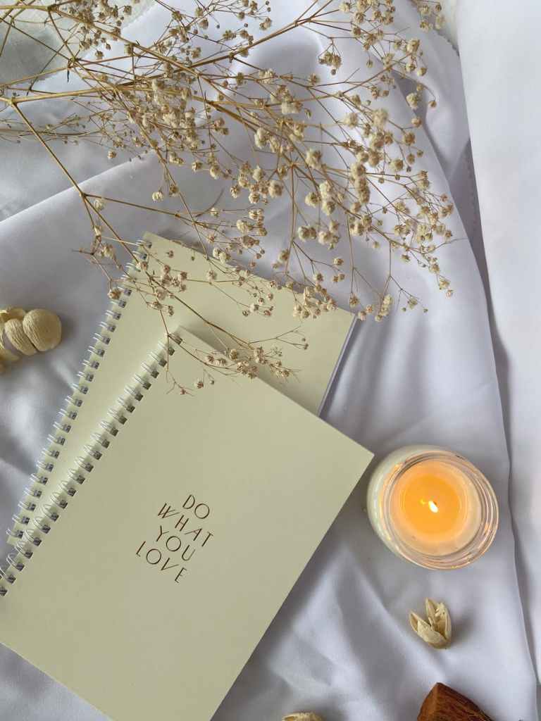 Notepads beside a burning orange candle upon a white table cloth.